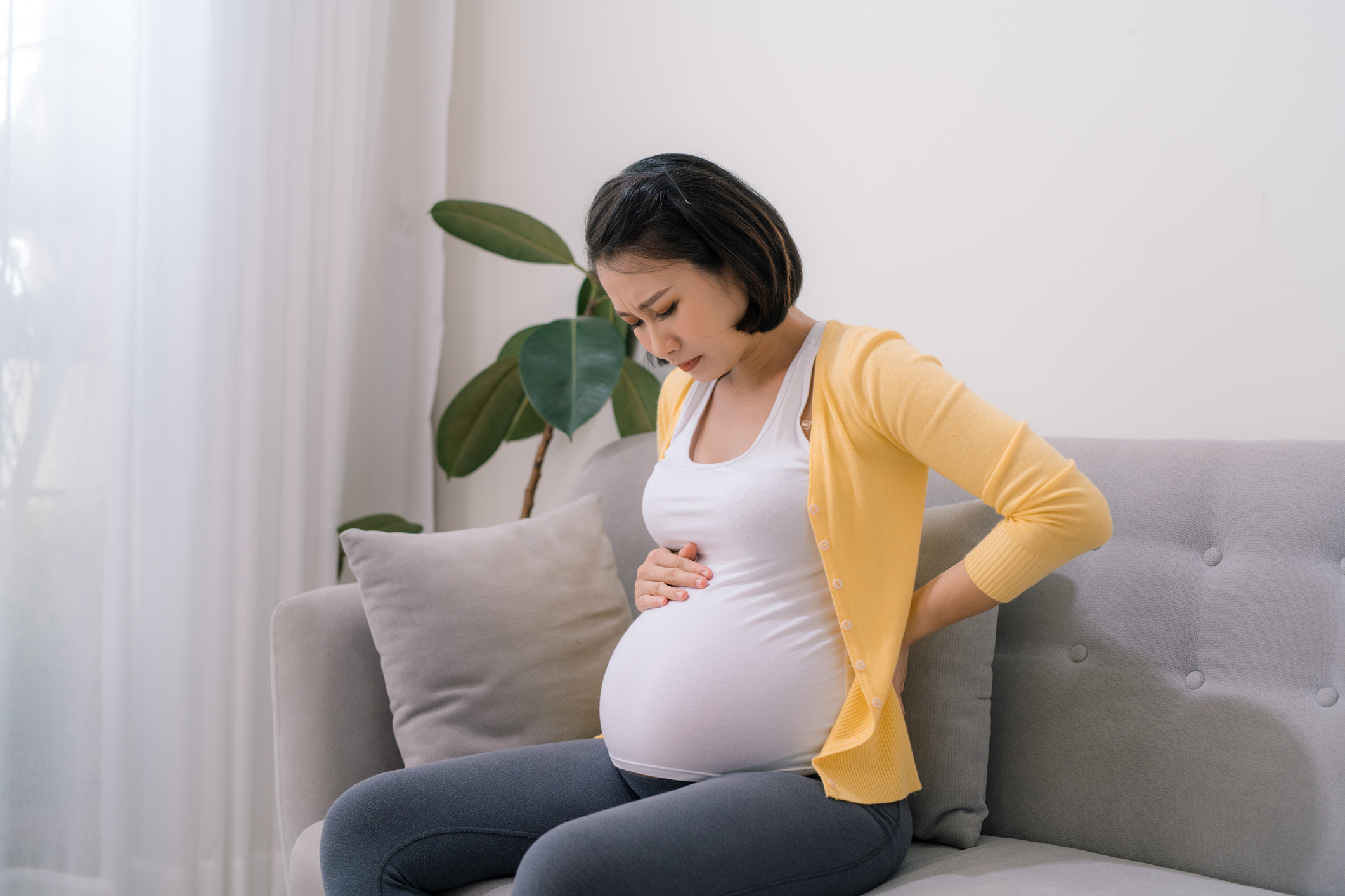 Pregnant woman experiencing discomfort sitting on the couch